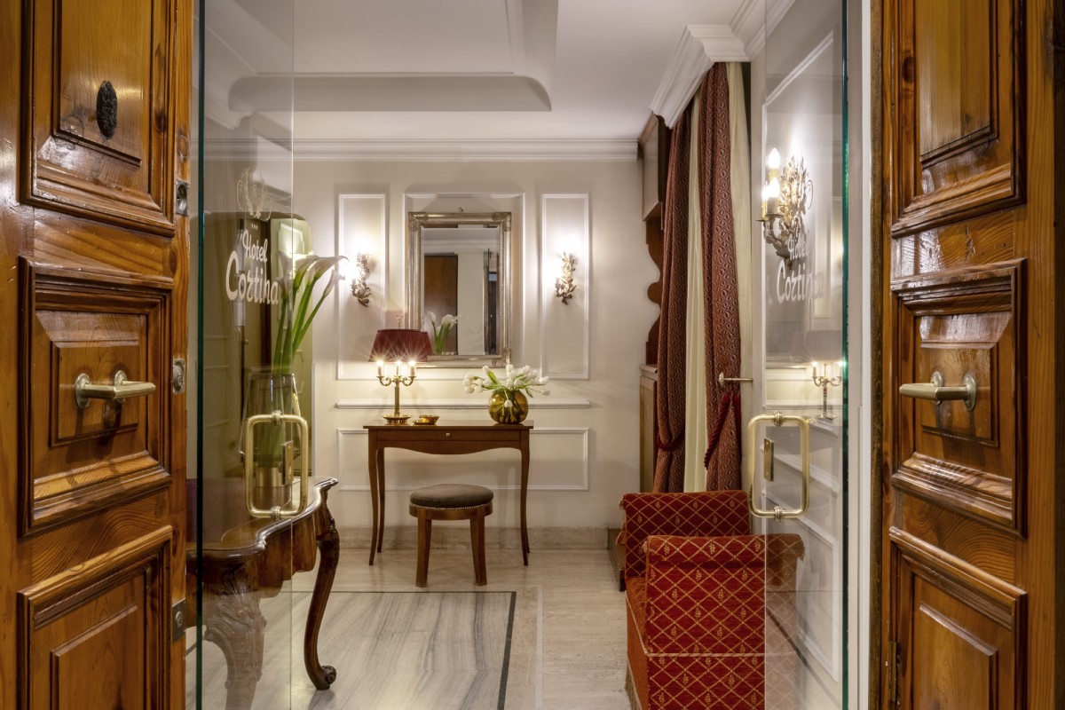 Interior view of the lobby at Hotel Cortina in Rome, featuring open arches that reveal the space, marble floors, and a three-bulb period lamp - Hotel Cortina, BZAR hotels in Rome